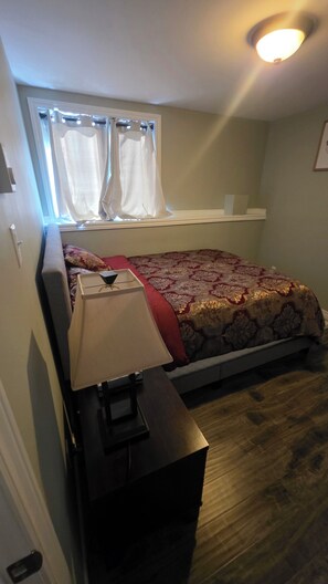 A bedroom with a bed, a bedside table, a window with curtains, and a ceiling light.