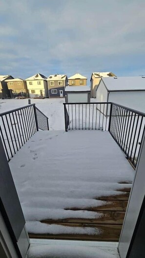 A snow-covered deck with a metal railing, leading to a building with multiple windows.