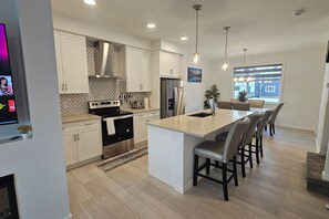 A modern kitchen with white cabinetry, stainless steel appliances, and a central island with bar stools.