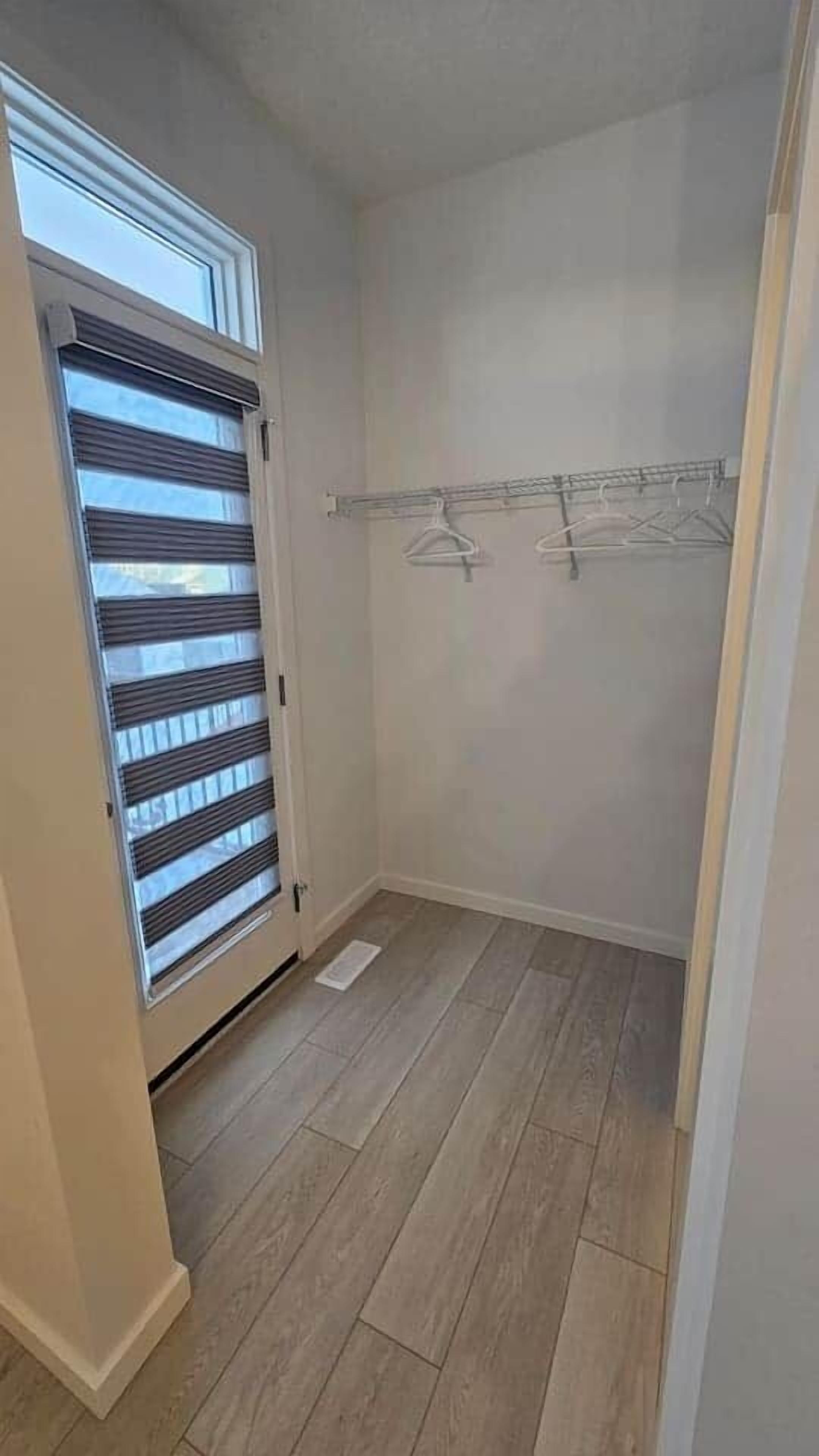 A walk-in closet with a sliding door, a wooden floor, and a metal drying rack.