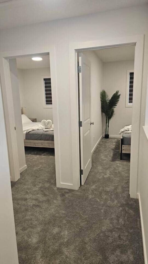 A bedroom with a bed, a nightstand, a potted plant, and a window with blinds.