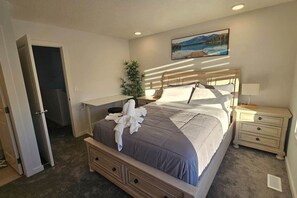 Une chambre à coucher avec un lit, des tables de chevet, un bureau, une plante et un tableau au mur.
