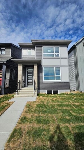 A modern two-story residential building with a front entrance, a covered porch, and a well-maintained lawn.