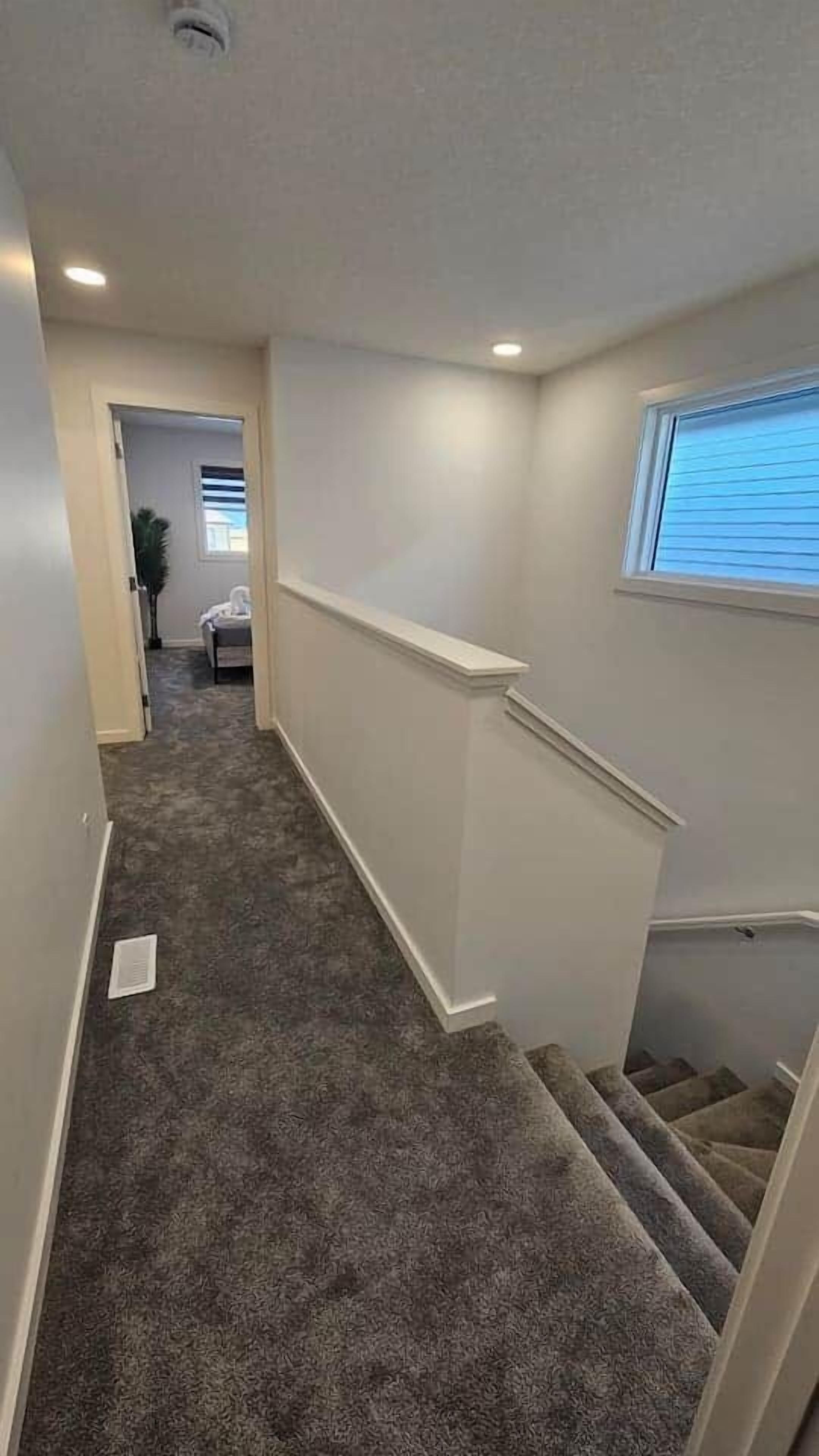 A carpeted stairway with a handrail, a window with blinds, and a door leading to another room.