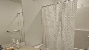 Casa de banho com sanita, lavatório, espelho e zona de duche.