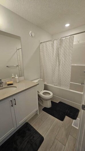 Et badeværelse med toilet, vask, spejl og bruseniche.