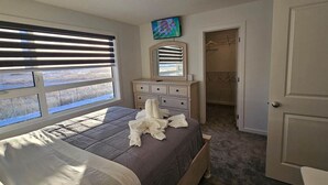 Quarto com cama, penteadeira, espelho e televisão na parede.