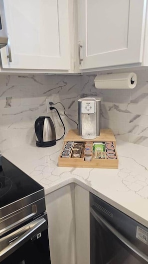 A kitchen with white cabinets, a coffee maker, a kettle, and a wooden tray with various items. - Luxury suite with 2-bedroom and 2 beds + Free Wifi (Calgary)