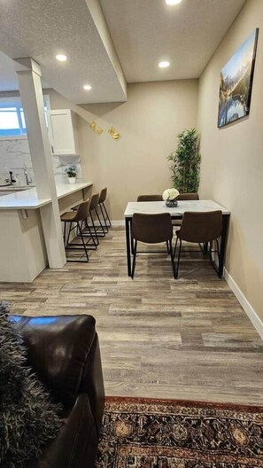 A dining area with a table and chairs, a kitchen area with a counter and chairs, and a patterned rug on the floor. - Luxury suite with 2-bedroom and 2 beds + Free Wifi (Calgary)
