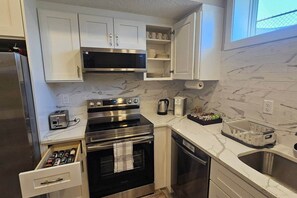 A compact kitchen with white cabinets, a stainless steel refrigerator, a microwave, an oven, a toaster, and a dish rack. - Luxury suite with 2-bedroom and 2 beds + Free Wifi (Calgary)