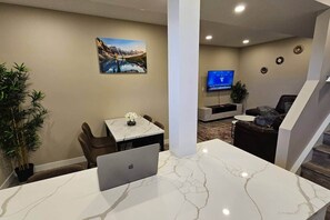 Un salon moderne doté d’un téléviseur à écran plat, d’un coin repas avec une table et des chaises, et d’un escalier menant à un autre niveau.