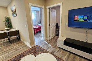 A modern living room with a flat-screen TV, a dining area with a table and chairs, and a hallway leading to a bedroom. - Luxury suite with 2-bedroom and 2 beds + Free Wifi (Calgary)