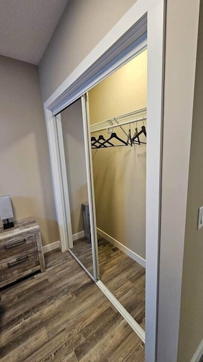 A walk-in closet with a sliding door, a wooden floor, and a metal rack for hanging clothes. - Luxury suite with 2-bedroom and 2 beds + Free Wifi (Calgary)