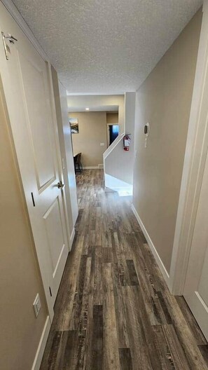 A hallway with wooden flooring, white walls, and a door on the left. - Luxury suite with 2-bedroom and 2 beds + Free Wifi (Calgary)