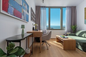 A modern living room with a desk, a green sofa, a view of the sea, and a painting on the wall. - Blue Elegant Suite (Thessaloniki)