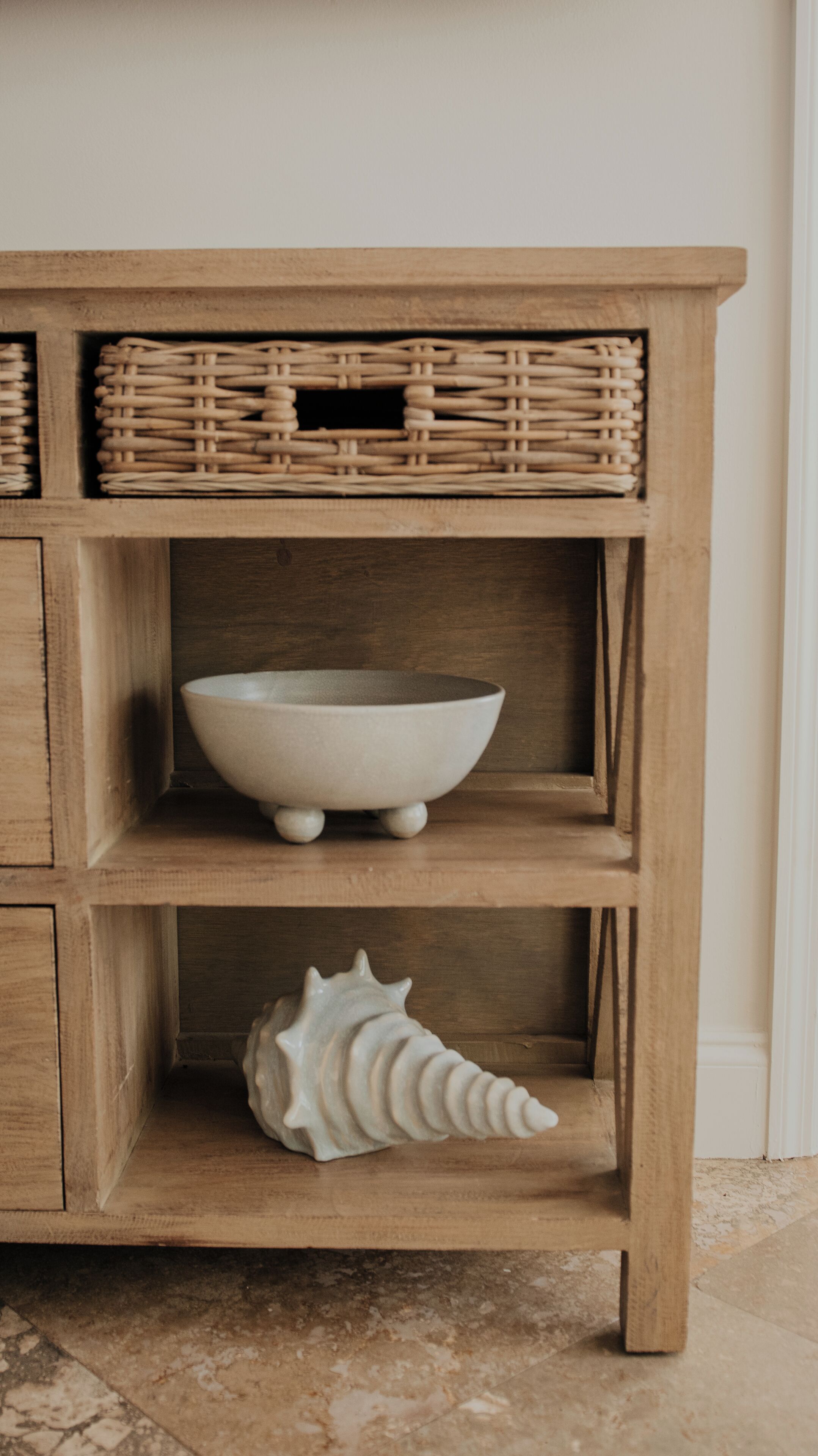 A wooden shelf with a woven basket, a ceramic bowl, and a seashell.