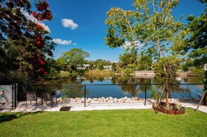 A fenced outdoor area with a pond, trees, and a grassy foreground. - Cozy 2-bedroom house in lovely Naples with private courtyard for relaxing stays. (Naples)