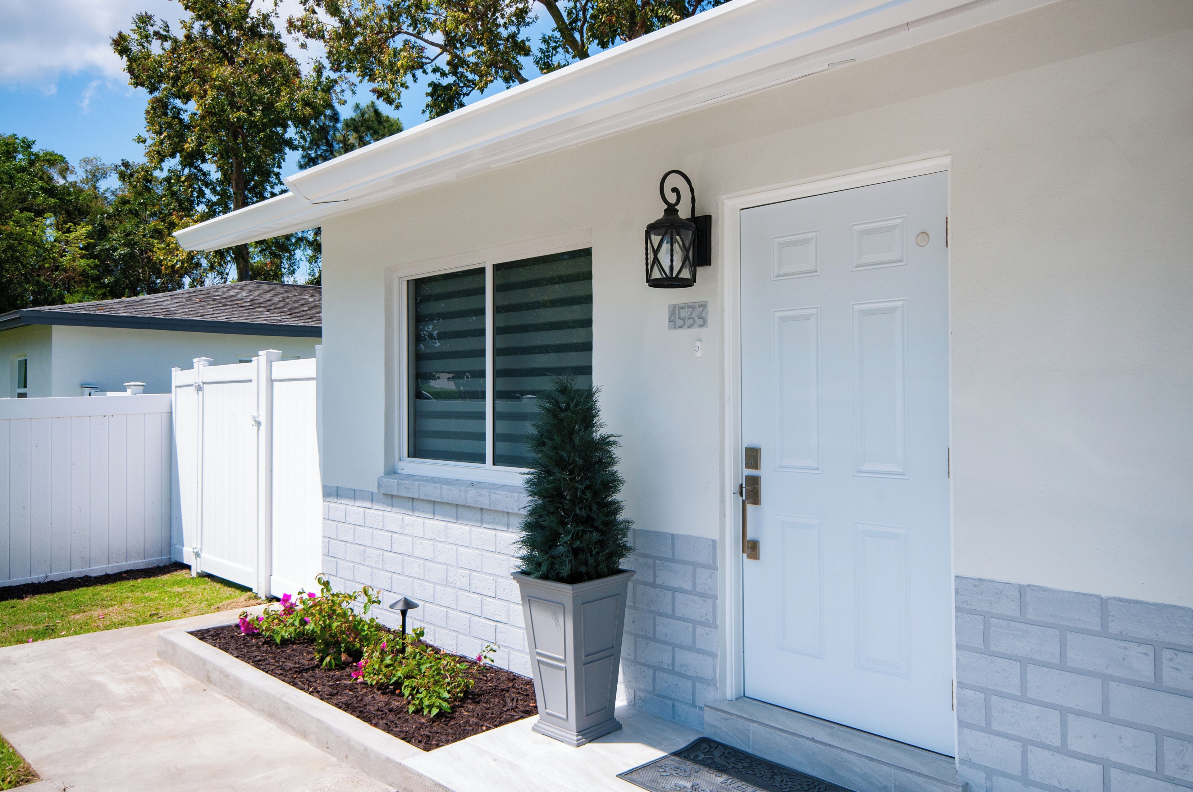 A residential house with a white exterior, a mailbox, a small potted plant, and a door with a number plate.