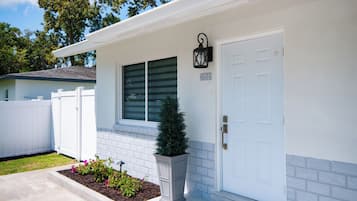 A residential house with a white exterior, a mailbox, a small potted plant, and a door with a number plate.