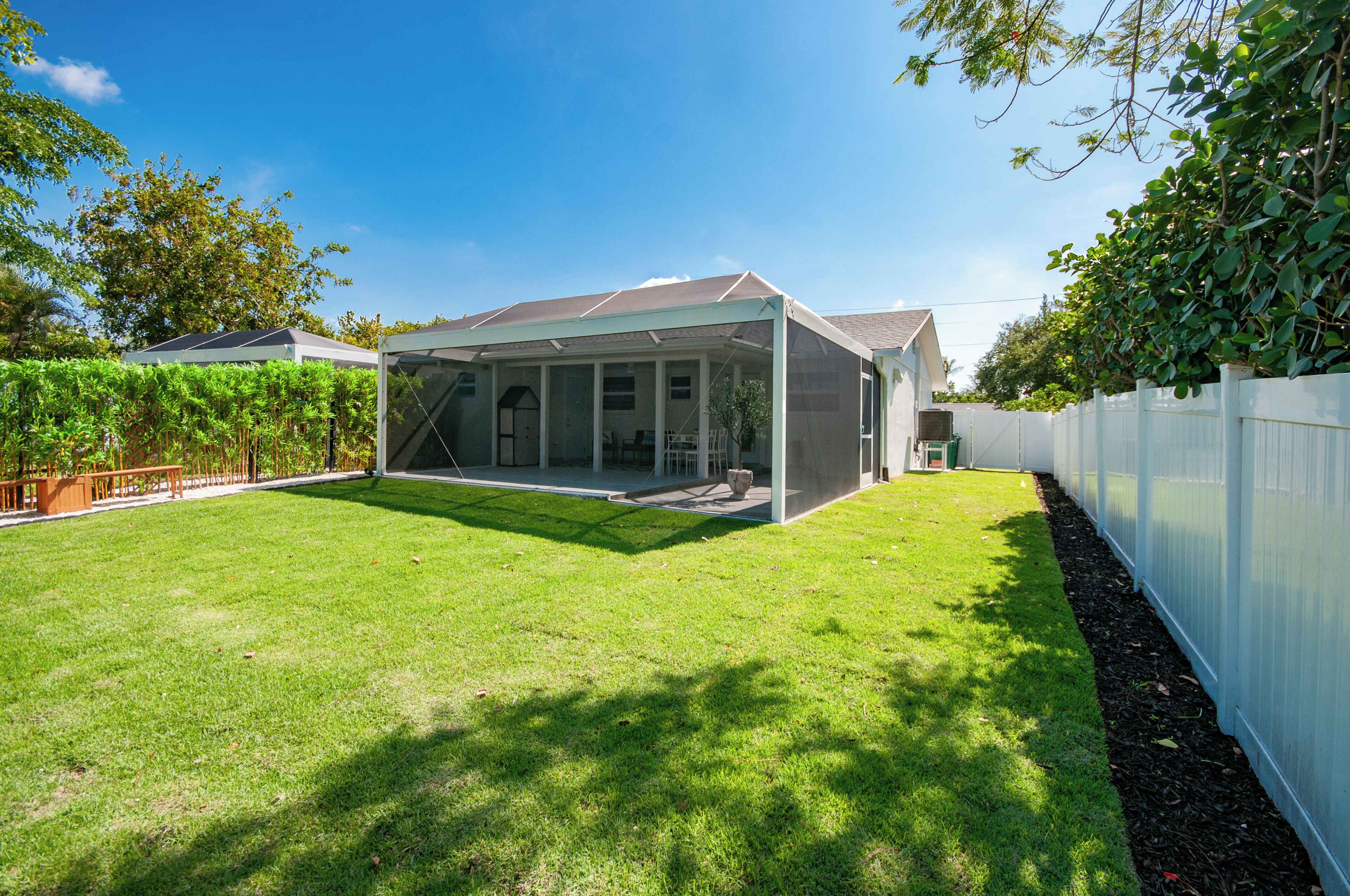 A house with a covered patio area, a fenced yard, and a variety of plants.
