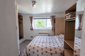 Ein Schlafzimmer mit einem Bett, einem Kleiderschrank, einem Fenster mit Vorhängen und einer Deckenleuchte.