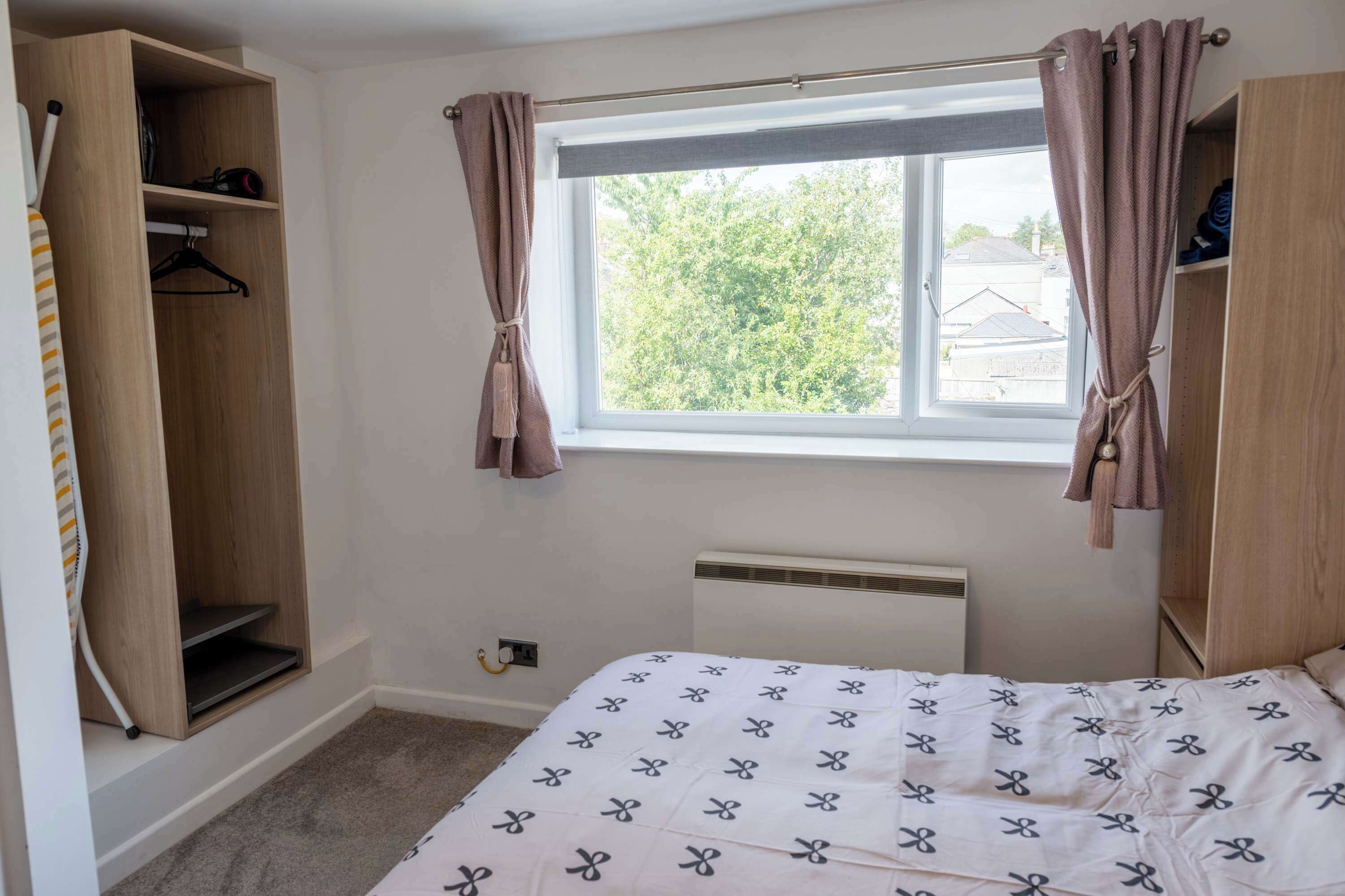 A bedroom with a bed, a window with curtains, a radiator, and a wardrobe.