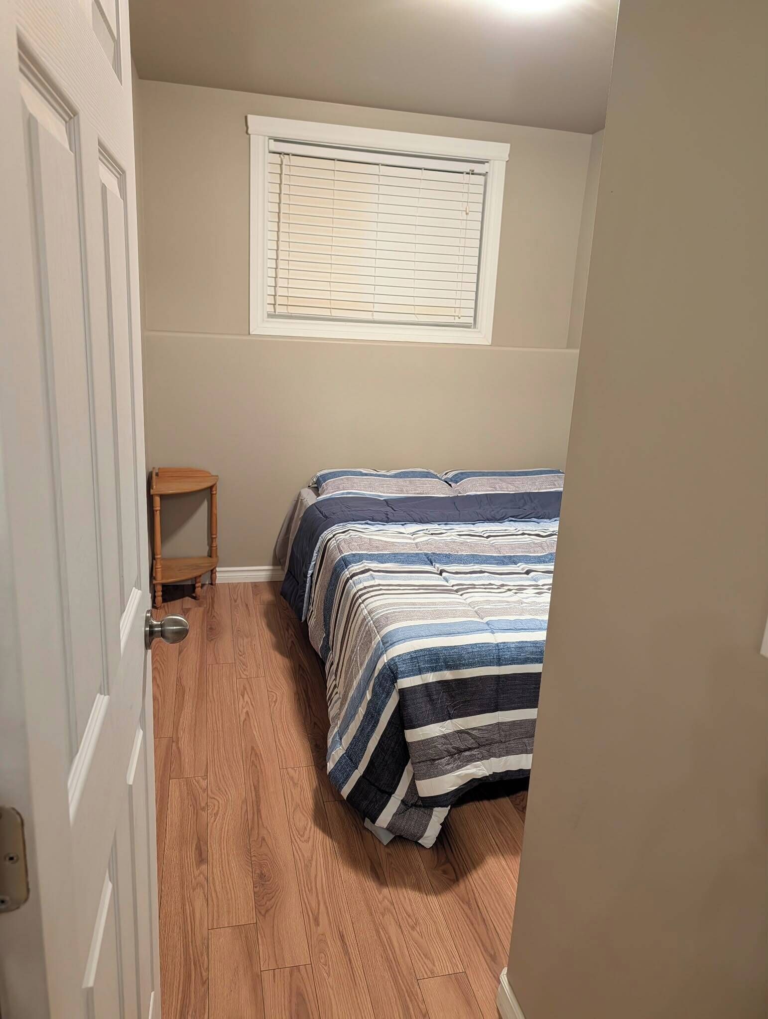 Una habitación pequeña con una cama, una silla de madera y una ventana con persianas.