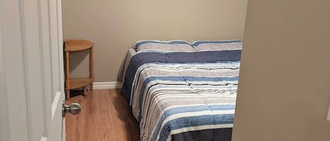 Een kleine kamer met een bed, een houten stoel en een raam met zonwering.