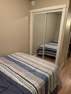 A bedroom with a bed, a mirror, and a wardrobe. - Modern two bedroom legal suite in beautiful evergreen, Saskatoon (Saskatoon)