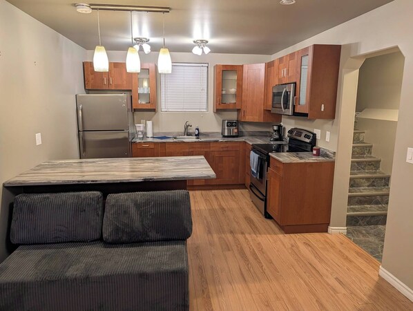 A compact kitchen with wooden cabinets, a refrigerator, a microwave, and a stove. - Modern two bedroom legal suite in beautiful evergreen, Saskatoon (Saskatoon)