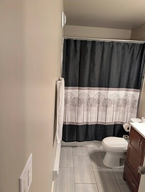 A bathroom with a toilet, a wooden cabinet, and a shower curtain with a tree pattern. - Modern two bedroom legal suite in beautiful evergreen, Saskatoon (Saskatoon)