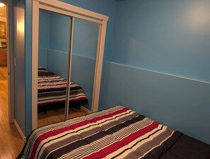 A bedroom with a mirrored wardrobe, a bed with striped bedding, and a blue wall. - Modern two bedroom legal suite in beautiful evergreen, Saskatoon (Saskatoon)