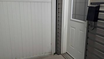 Ett garage med en vit dörr, ett betongsteg som leder upp till dörren och en metallanordning för att öppna garagedörren, placerad på höger sida.