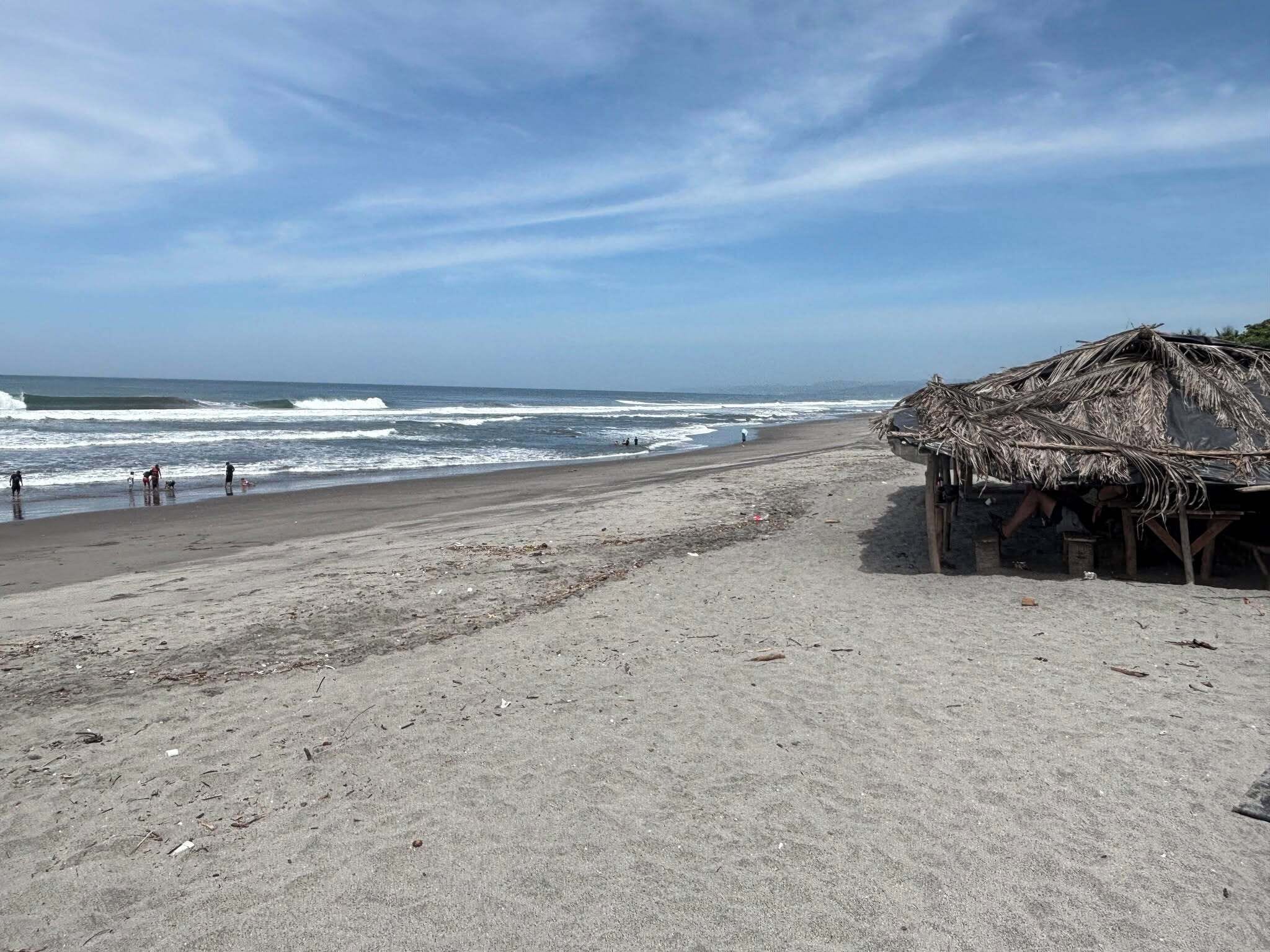 Ein Strand mit einer strohgedeckten Struktur, Wellen und blauem Himmel.