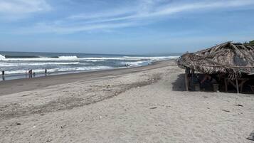 Ein Strand mit einer strohgedeckten Struktur, Wellen und blauem Himmel.