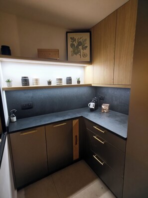 A modern kitchen with dark cabinetry, a countertop, and a shelf with various items. - Luxury Villa • Swimming Pool • View • Elevator (Falicon)