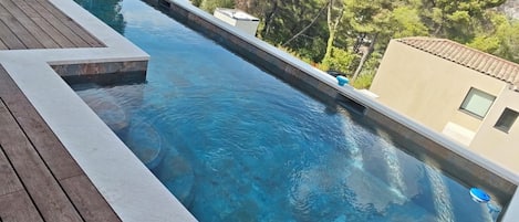 A rectangular swimming pool with clear blue water, surrounded by a wooden deck.