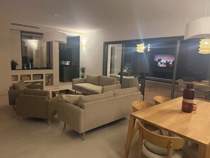 A modern living room with a sofa set, a dining table, and a TV screen displaying a sunset. - Luxury Villa • Swimming Pool • View • Elevator (Falicon)