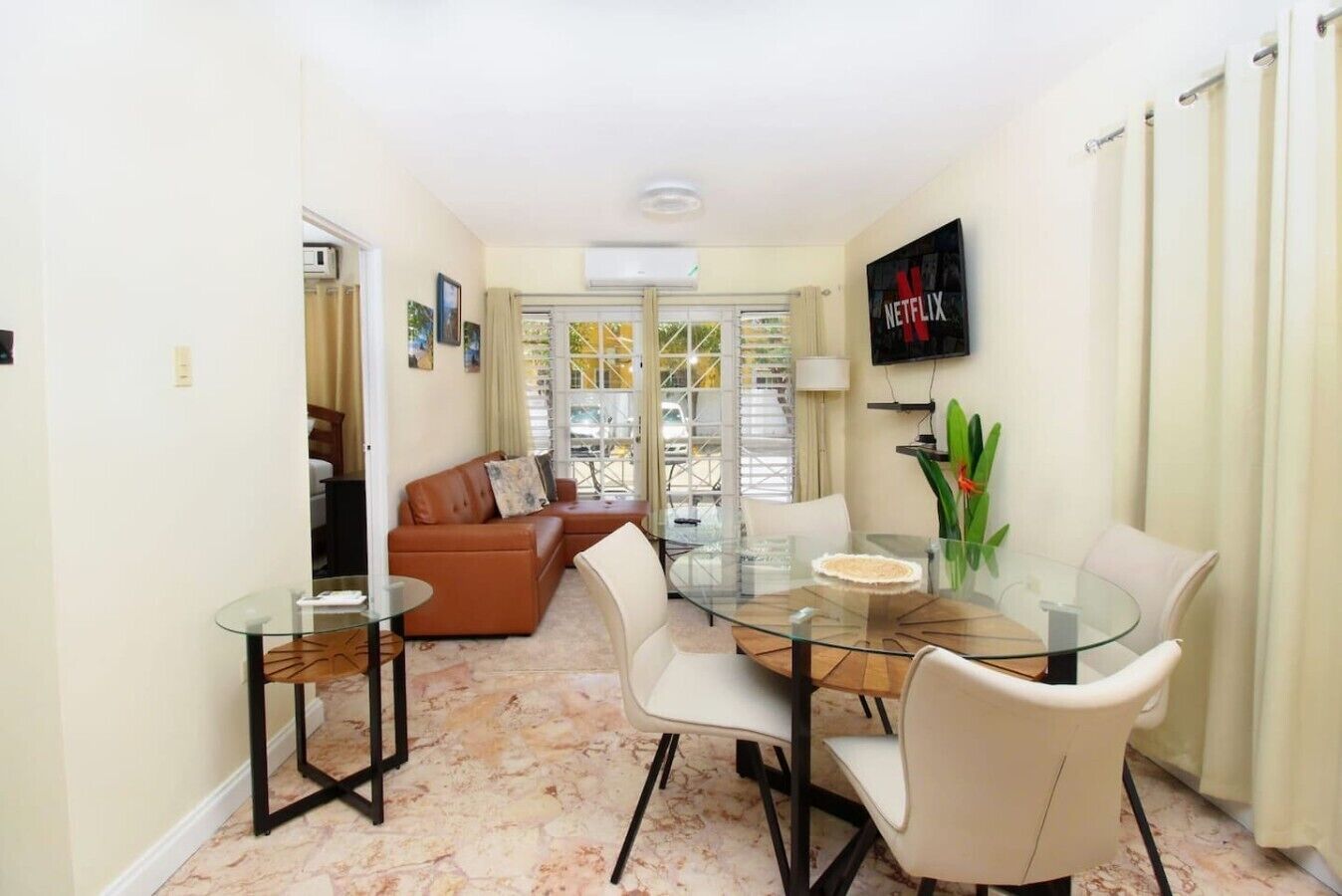 A dining area with a glass table, white chairs, and a sofa in the background.