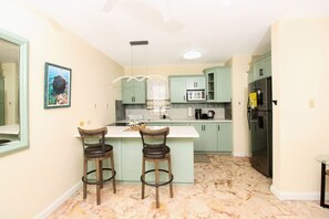A kitchen with a marble floor, two bar stools, a central island, and a refrigerator. - Cozy one Bed across from Eatery and Pickle Ball (Kingston 6)