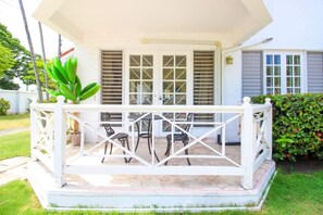 A covered outdoor seating area with a table and chairs, a potted plant, and a white railing. - Cozy one Bed across from Eatery and Pickle Ball (Kingston 6)