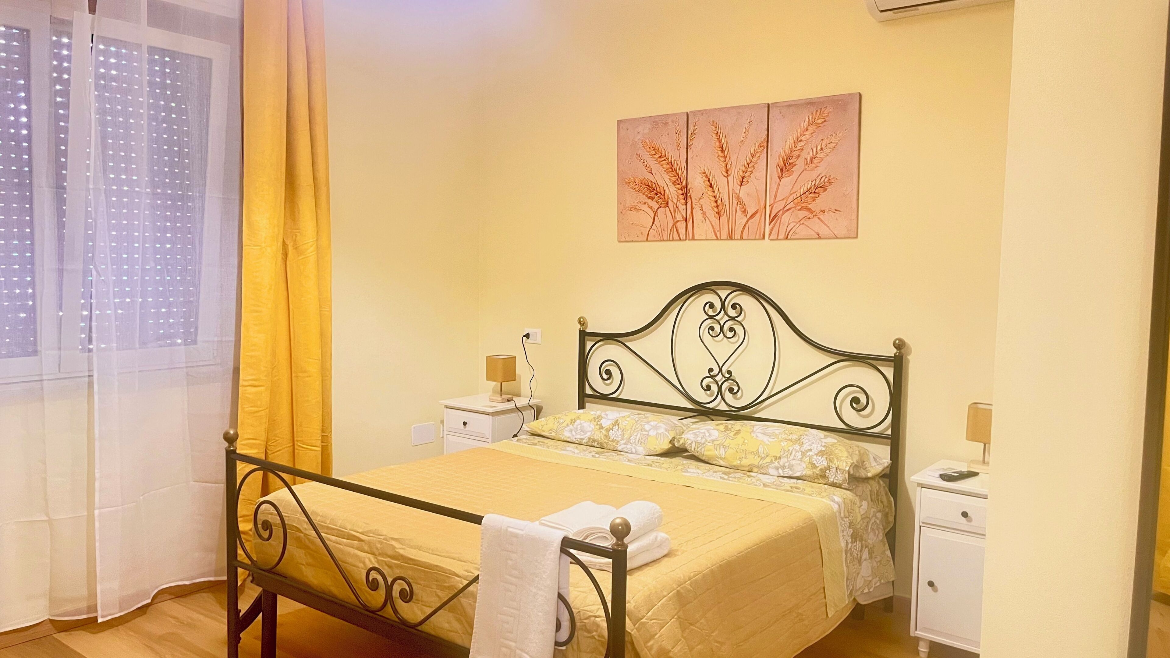 A bedroom with a bed, bedside tables, a window with curtains, and a wall art piece.