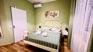 A bedroom with a bed, a bedside table, a nightstand, a wall-mounted air conditioner, and a door.