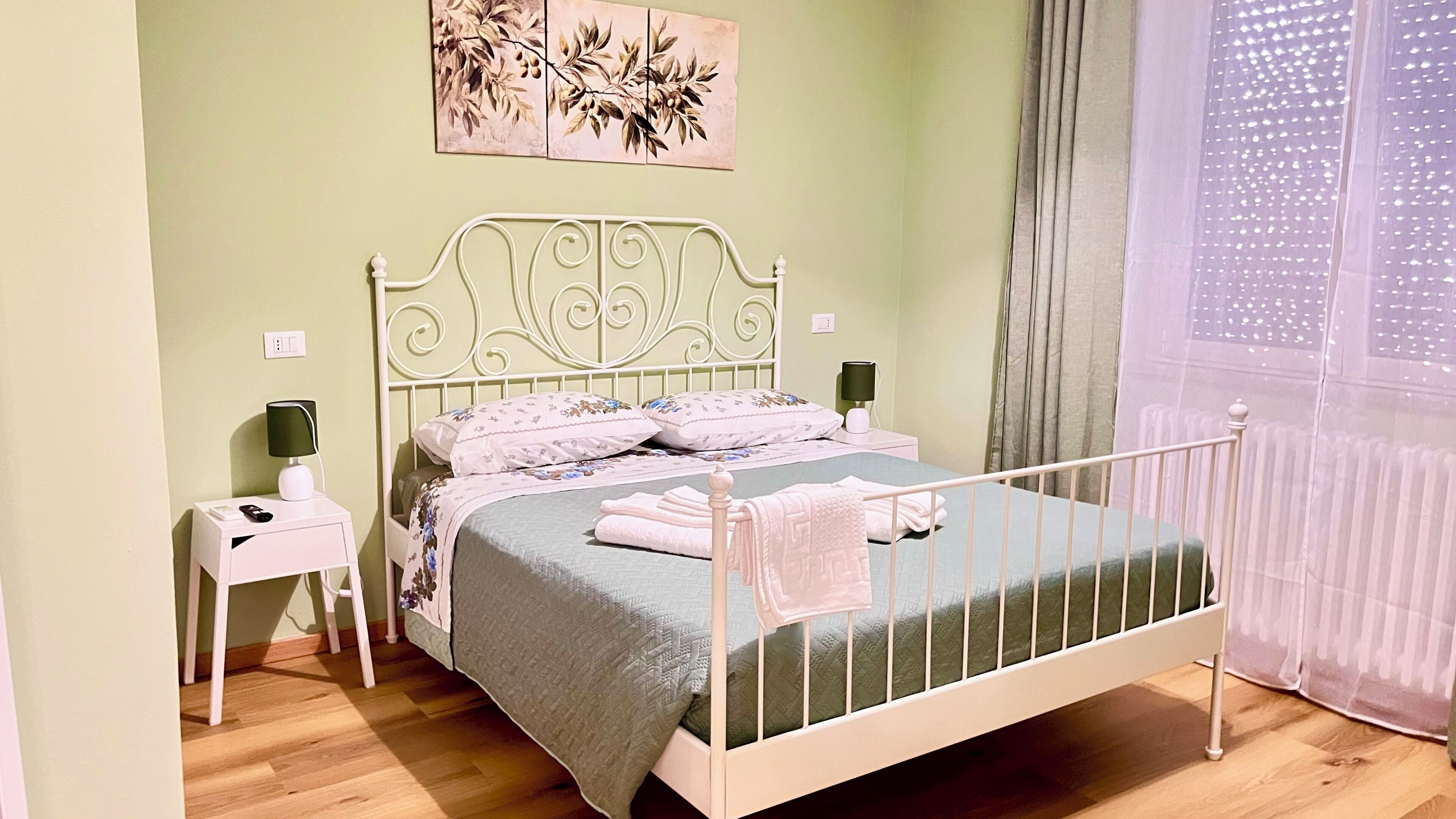 Una cama con estructura metálica, una mesita de noche con lámpara y una obra de arte colgada en la pared.
