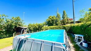 A rectangular swimming pool with a metal ladder, surrounded by a fence and greenery.