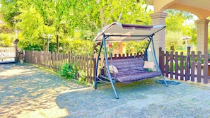 A garden with a swing set, a paved pathway, and a wooden fence.
