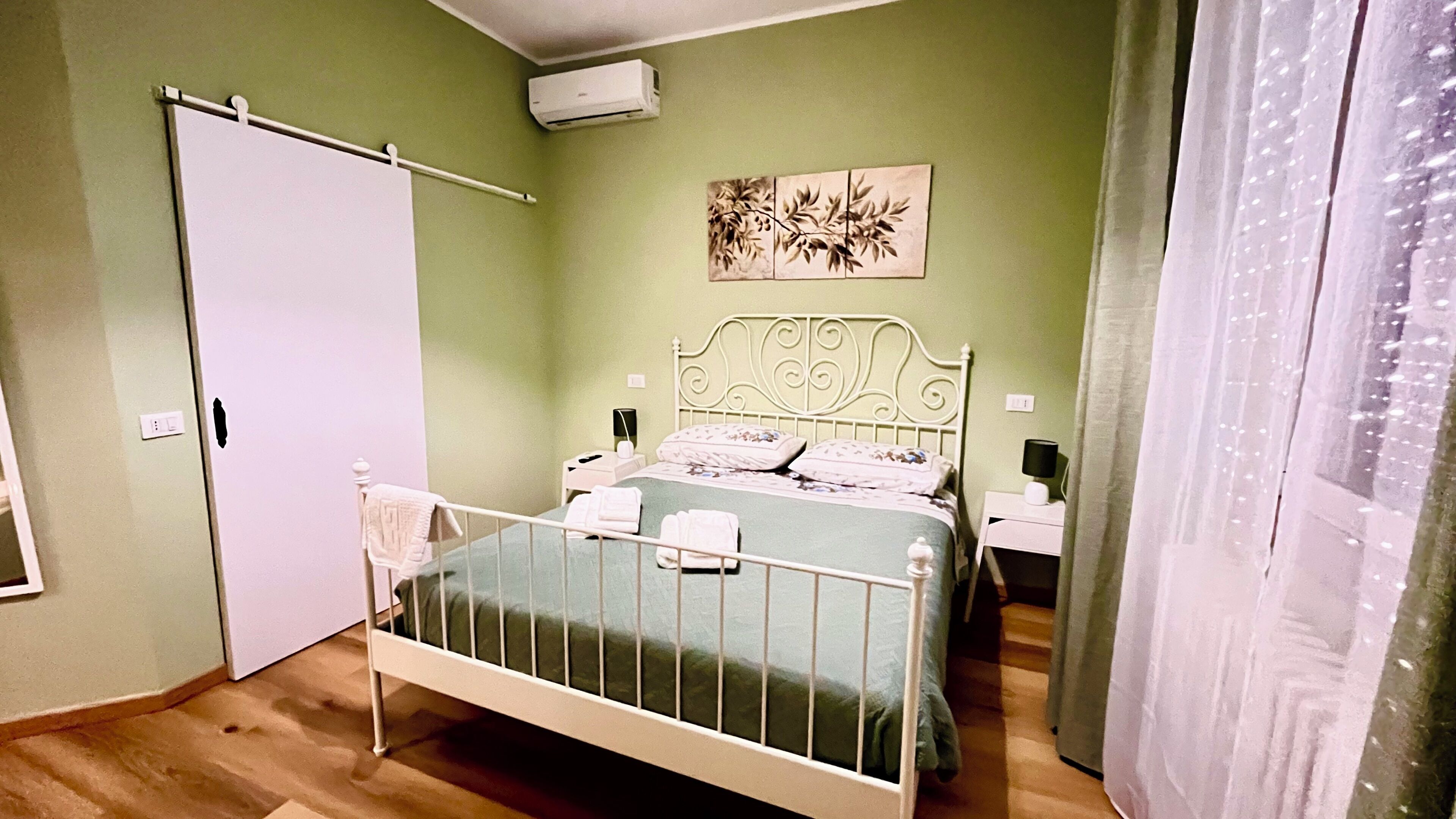 Un dormitorio con una cama, una mesita de noche, aire acondicionado y una cortina.