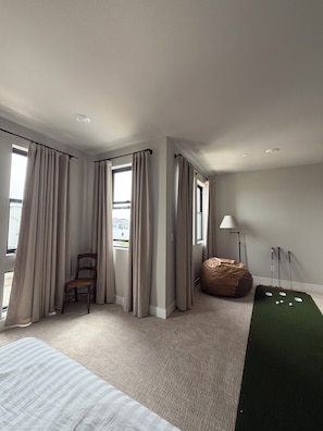 A modern hotel room with a large bed, a bean bag, a green putting mat, and a view of the city. - U.S. Open Retreat - Rooftop Condo Near Pebble Beach (Marina)