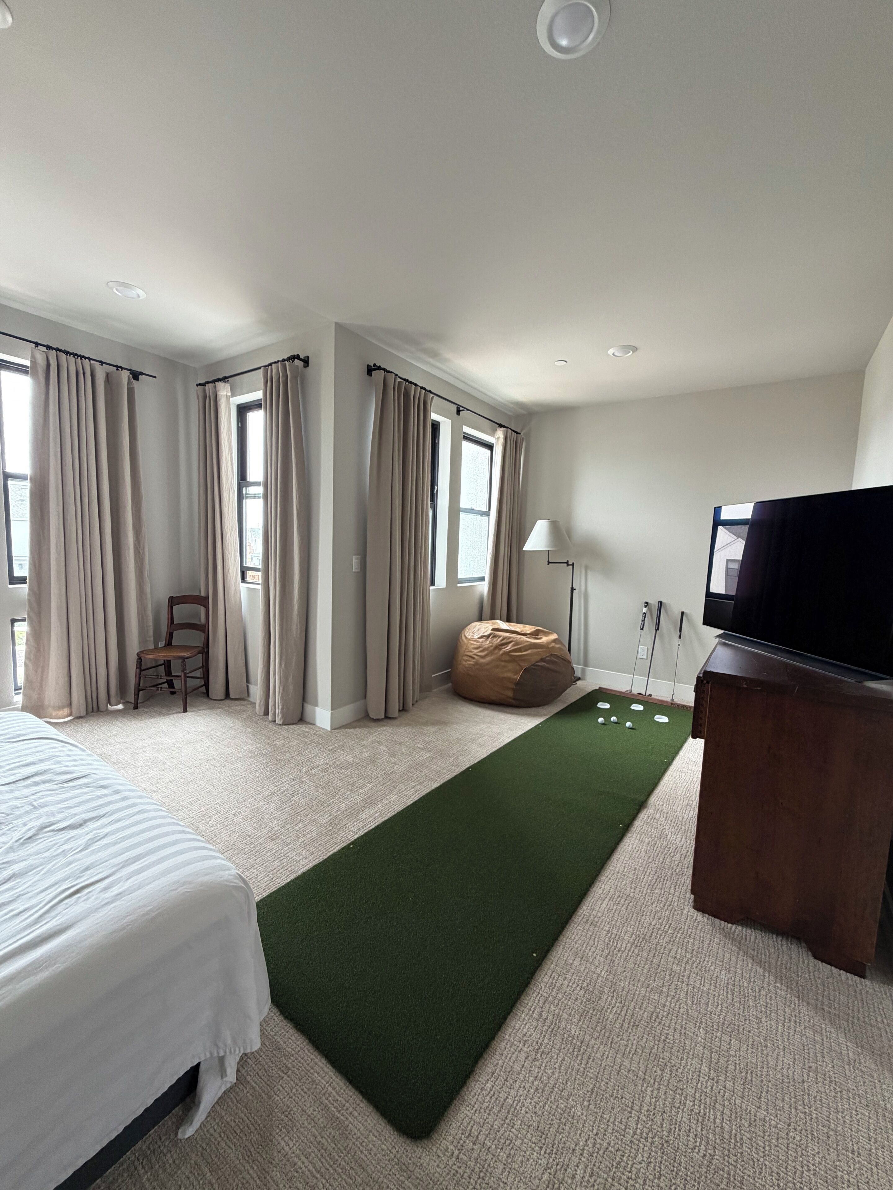 A hotel room with a bed, a bean bag, a TV, and a carpeted area.