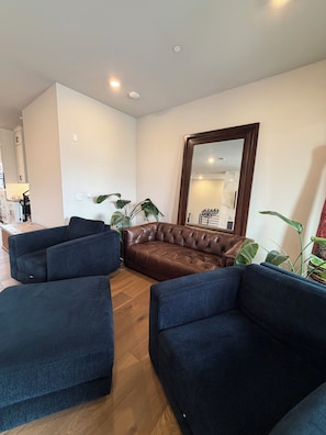 A living room with a brown leather sofa, two dark blue armchairs, and a large mirror on the wall. - U.S. Open Retreat - Rooftop Condo Near Pebble Beach (Marina)